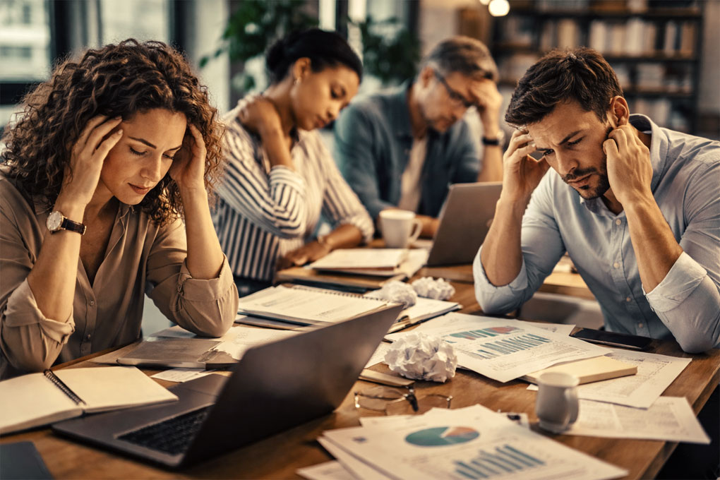 Equipo de personas trabajando que muestran síntomas de estrés y agotamiento psíquico