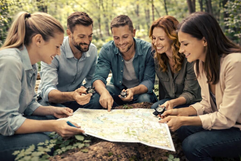Equipo de personas en actividad de coaching empresarial en plena naturaleza, resolviendo dinámica de orientación con brújulas y mapas.
